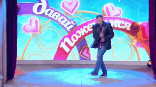 a man is dancing on a stage in front of a large screen that says " давай "
