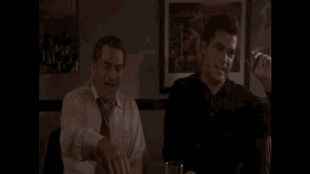 two men are sitting at a table in front of a picture of a man in a boxing ring .