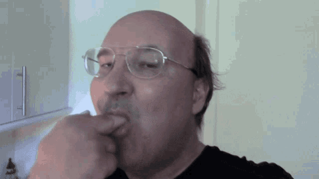 a bald man wearing glasses is licking his fingers