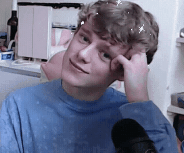 a young man in a blue shirt is sitting in front of a black microphone