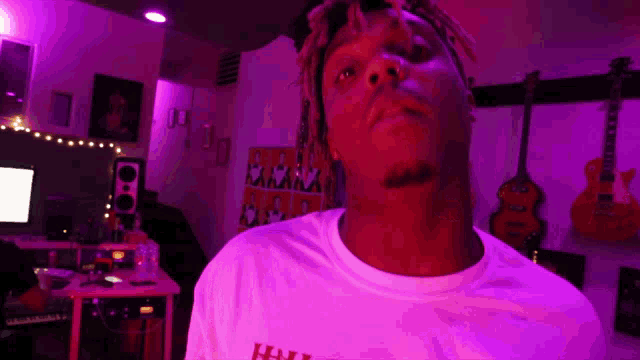 a man in a white t-shirt is standing in a room with purple lights .
