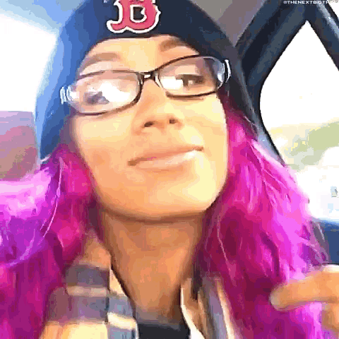 a woman with pink hair and glasses is wearing a beanie and a scarf .