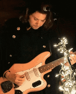 a woman in a black coat is playing a guitar