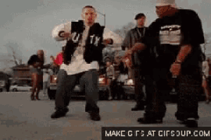 a group of men are dancing in a parking lot and one of them is wearing a vest that says u.tx