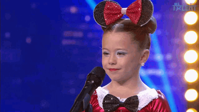 a little girl is singing into a microphone on a talent show