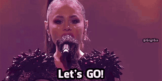 a woman is singing into a microphone with the words `` let 's go '' written on the screen .