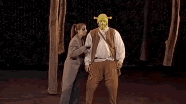 a man in a shrek costume stands next to a woman on a stage