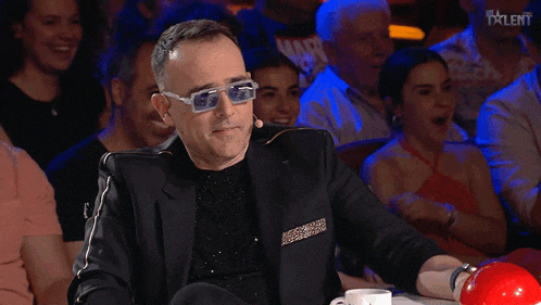 a man wearing sunglasses is sitting at a table with a red ball in front of him and a sign that says talent on it