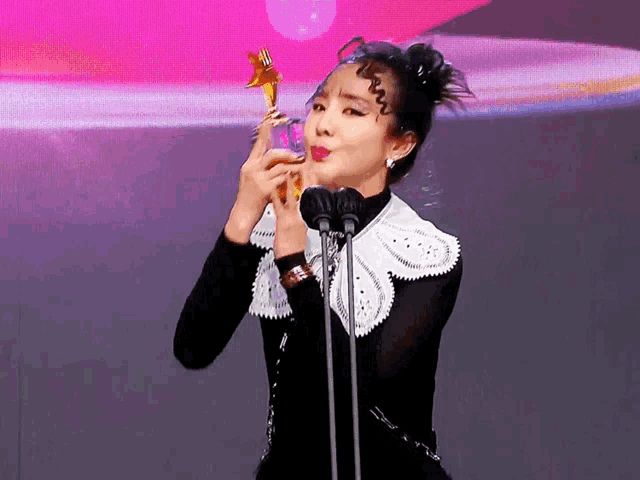 a woman is holding a trophy in front of a microphone with a star on it