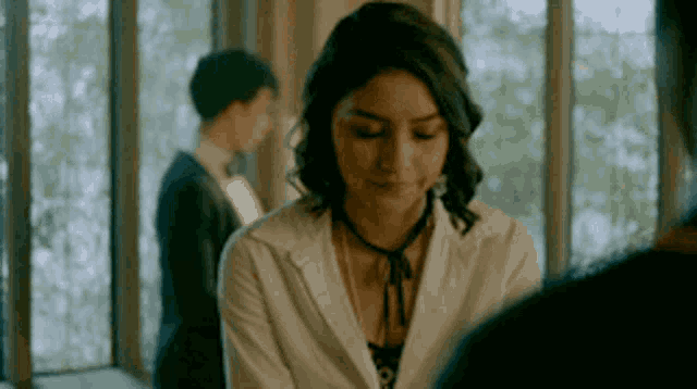 a woman in a white jacket is standing in front of a window .