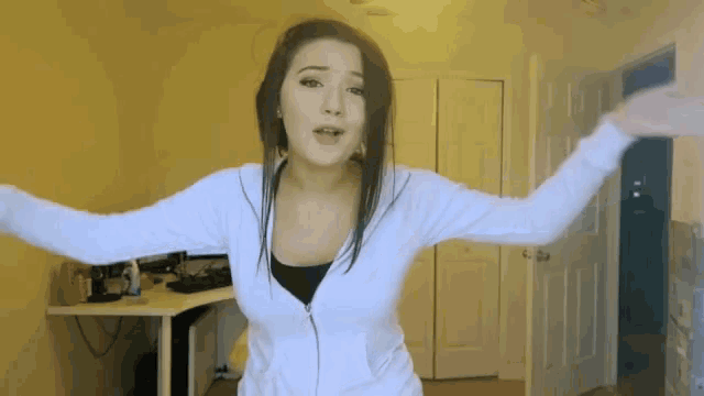 a woman in a white jacket is dancing in a room with her arms outstretched