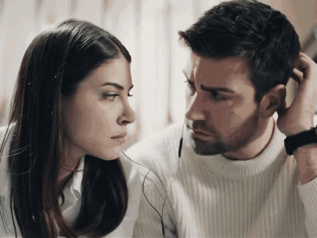 a man and a woman are looking at each other and the man has headphones in his ears