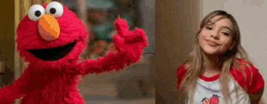 a woman is standing next to a stuffed animal that is elmo from sesame street .