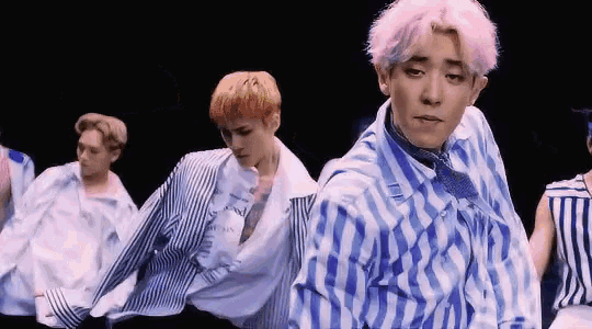 a group of young men are dancing together in a dark room . one of the men is wearing a blue and white striped shirt .
