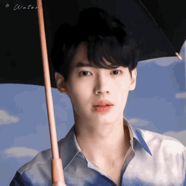 a young man holding a black umbrella with water written on the bottom right