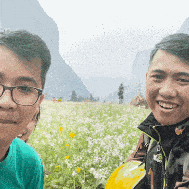 two men are posing for a picture in a field of flowers and one of them is wearing a jacket that says the north face