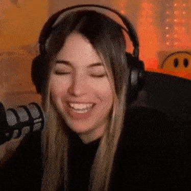a woman wearing headphones is smiling and laughing in front of a microphone .