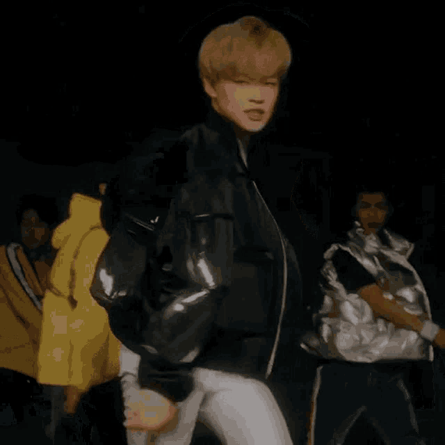 a young man with blonde hair is wearing a white shirt and a black jacket and making a funny face .