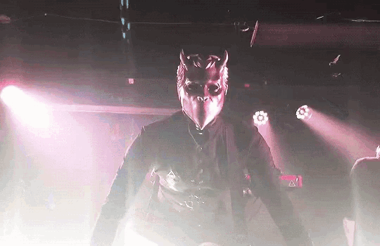 a man in a mask is standing on a stage in front of a purple light .