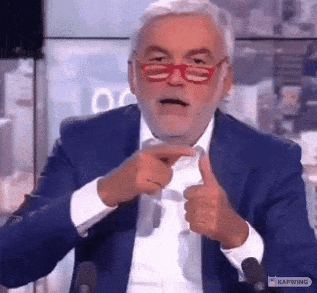 a man in a blue suit and red glasses is giving a thumbs up sign