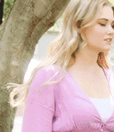 a woman in a pink sweater is standing next to a tree
