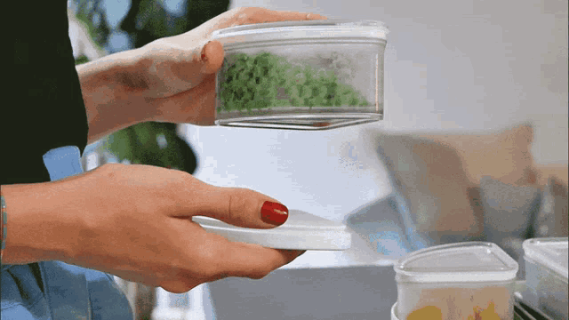 a woman with red nails is holding a clear plastic container with greens in it
