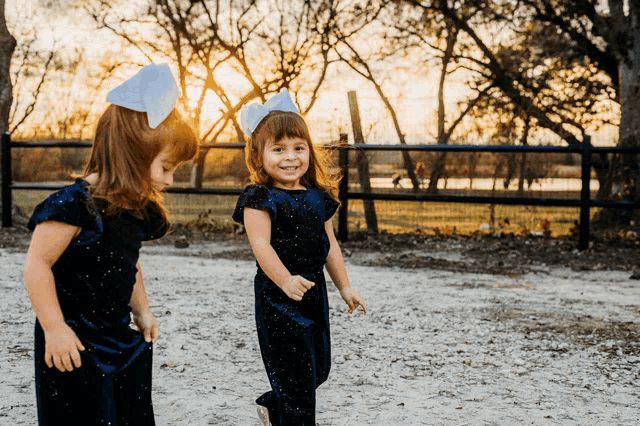 two little girls wearing blue jumpsuits with bows on their heads