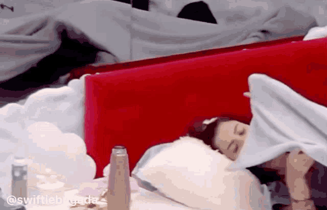 a woman is sleeping in a bed with a red headboard and white sheets