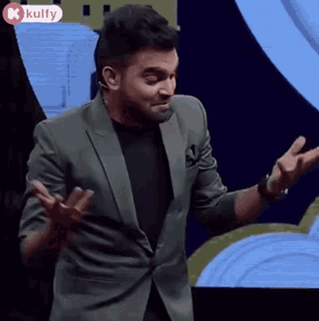 a man in a green suit and black shirt is making a funny face with his hands outstretched .
