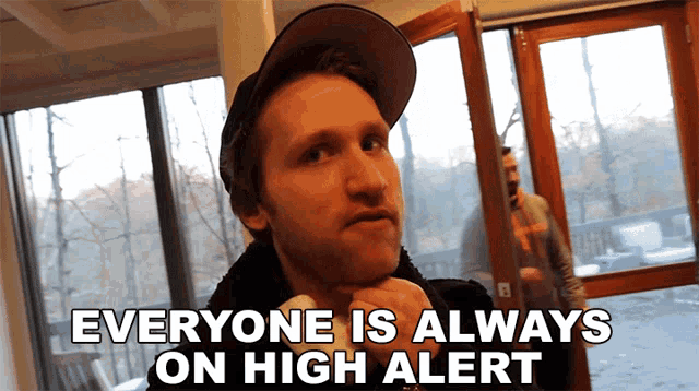 a man wearing a hat stands in front of a window with the words everyone is always on high alert below him