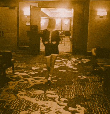 a woman in a black dress walks through a hallway with a patterned rug