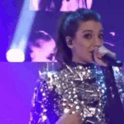 a woman is singing into a microphone on stage .