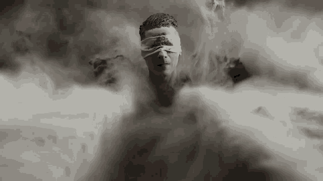 a man with blindfolds on his eyes is surrounded by clouds .