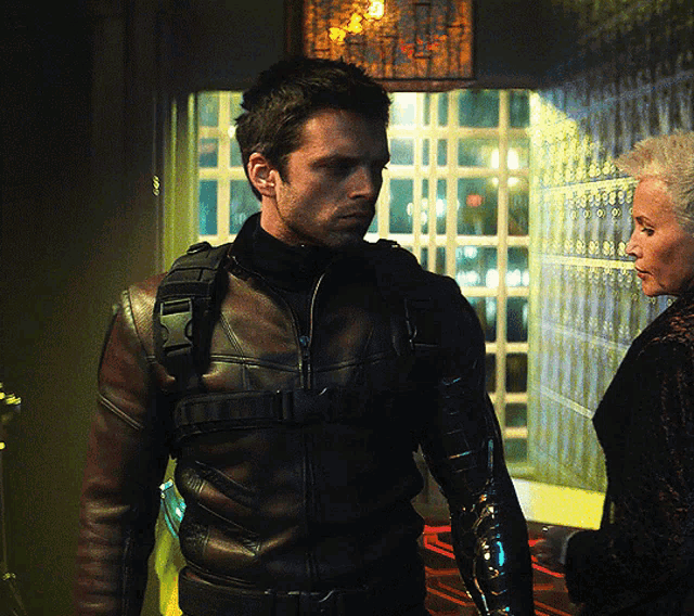 a man in a leather jacket stands next to a woman in a black coat