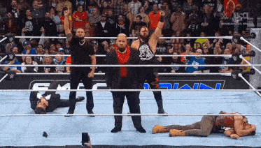 a group of men are standing in a wrestling ring with one man laying on the ground .