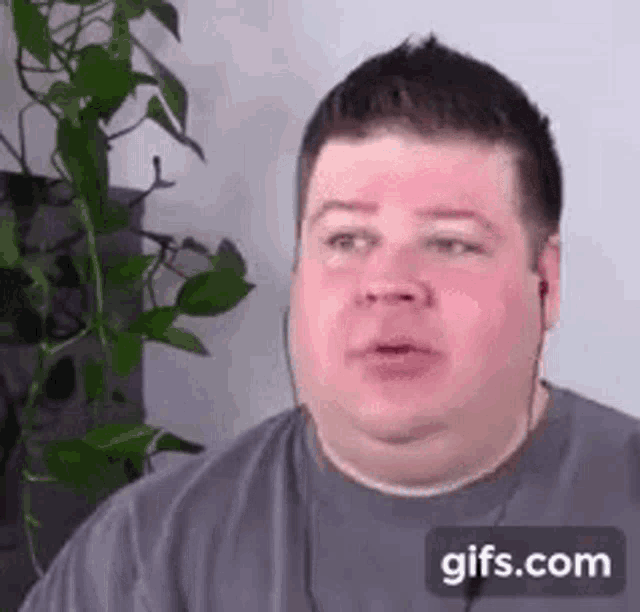 a man wearing headphones is sitting in front of a plant and making a funny face .
