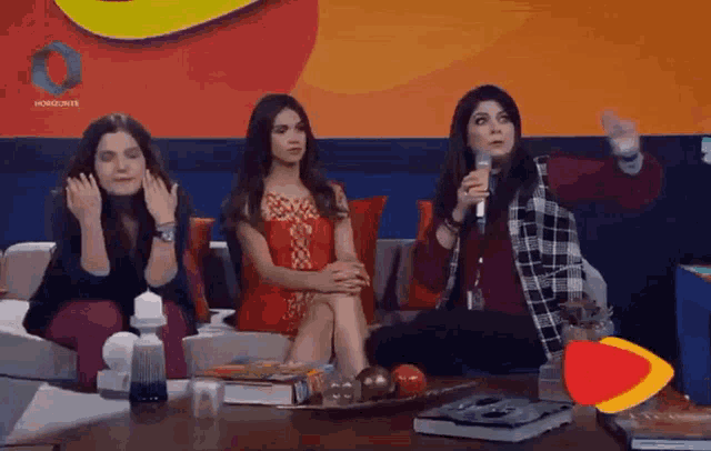 three women are sitting on a couch and one is holding a microphone in front of a horizonte sign