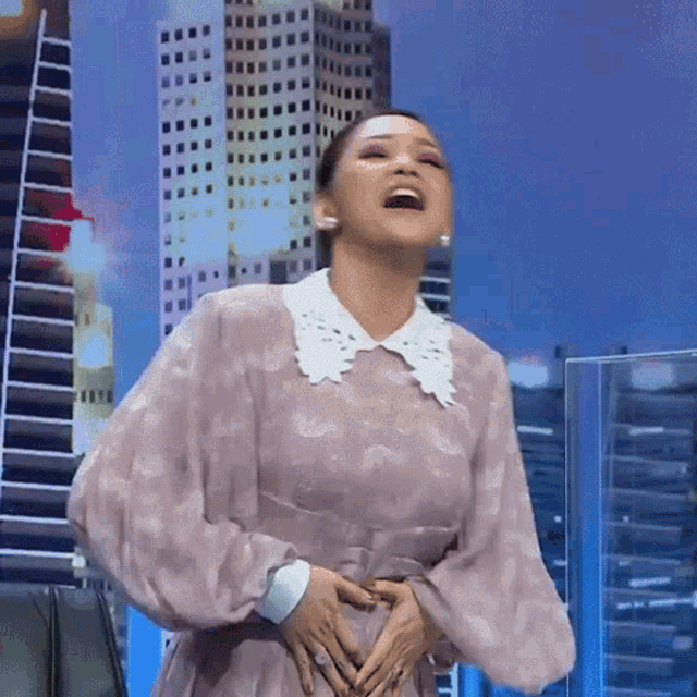 a woman in a pink dress with a white collar is holding her belly and laughing .