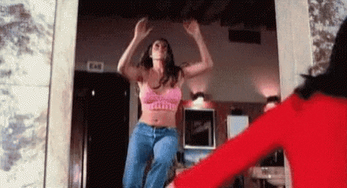 a woman in a pink bra and jeans is dancing in a room with a woman in a red shirt .