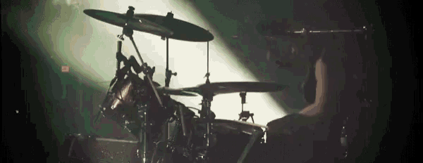a man is playing drums in a dark room with a spotlight behind him