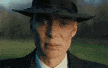 a man wearing a hat and a suit looks at the camera