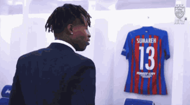 a man in a suit stands in front of a jersey that says sunareh 13