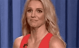a woman in a red dress is making a funny face while standing in front of a blue curtain .