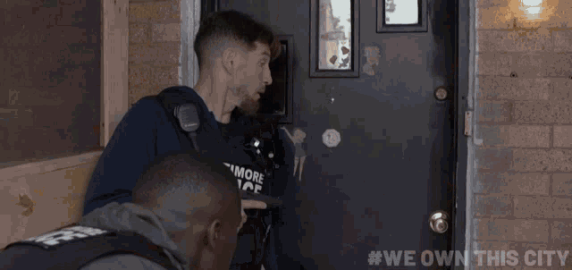 two men are standing in front of a door with #we own this city written on the bottom right
