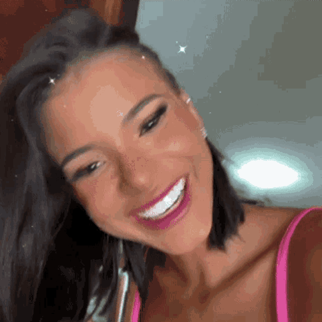 a woman in a pink tank top is smiling and taking a selfie with her phone .