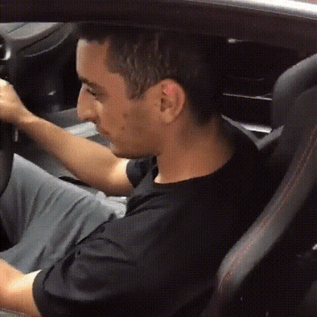 a man is sitting in the driver 's seat of a car and holding the steering wheel .