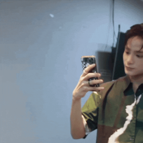 a man in a green shirt is holding a cell phone in his hand
