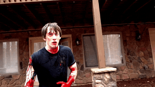 a man with blood on his face and hands stands in front of a stone wall