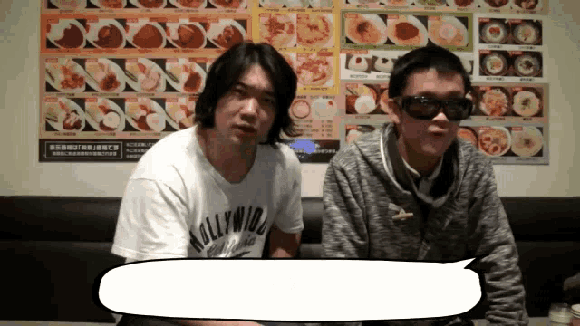 a man wearing a hollywood shirt sits next to a man wearing sunglasses