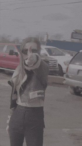 a woman wearing sunglasses and a jacket is standing in front of a parking lot
